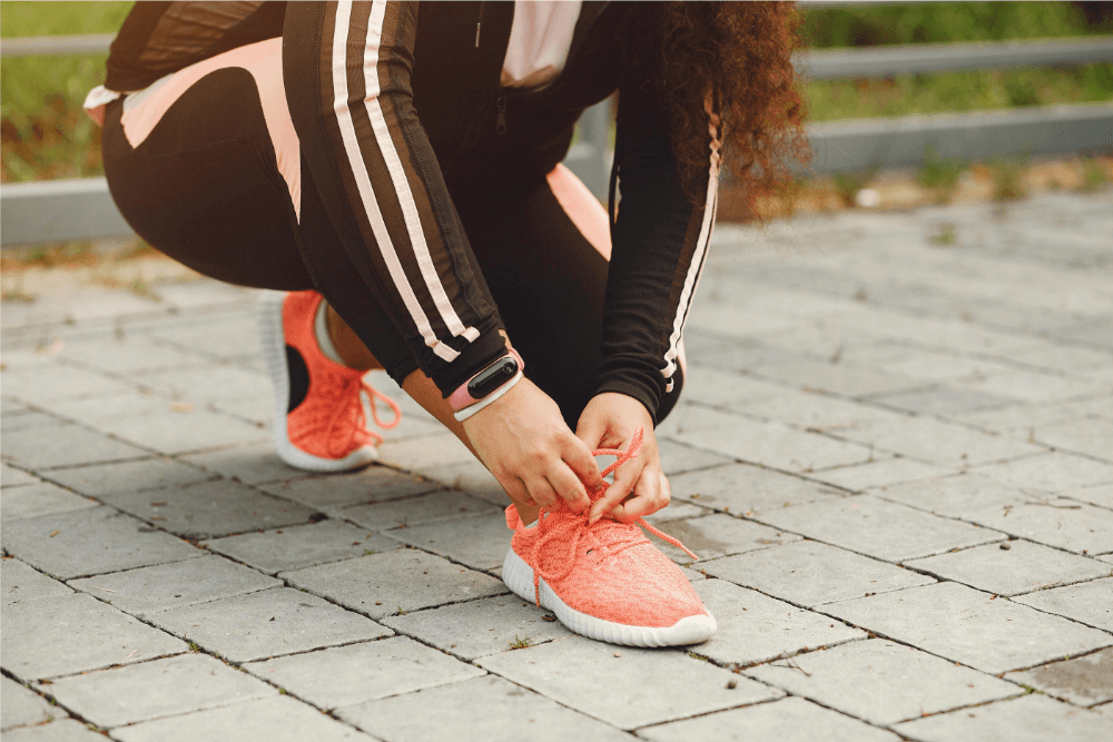 A woman kneels down to tie her running shoe.