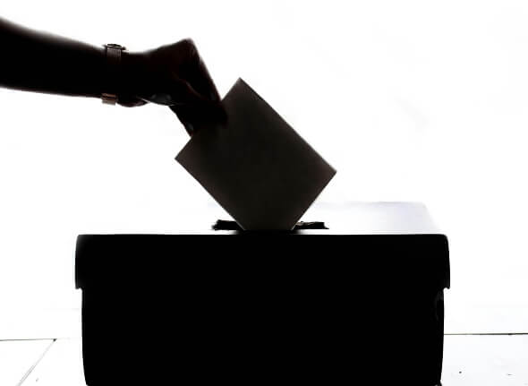 Decorative image of a hand placing a ballot paper in a box