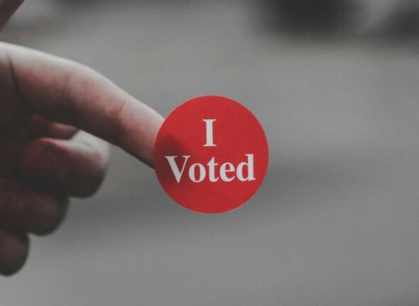 Decorative image of a red sticker with the white words I voted, stuck on the end of a finger