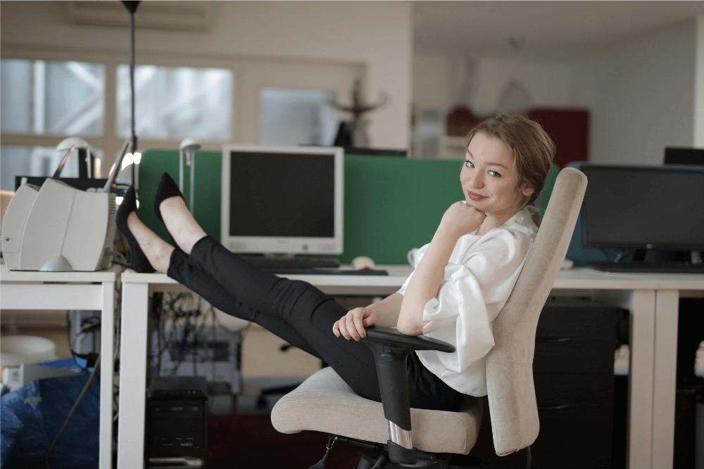 A young woman at work reclines in her chair with her feet on her desk.