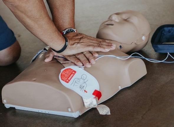 A person with 2 hands performing chest compressions on a medical dummy.