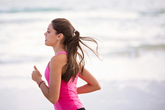 a young woman running along a beach wearing a bright pink sports vest