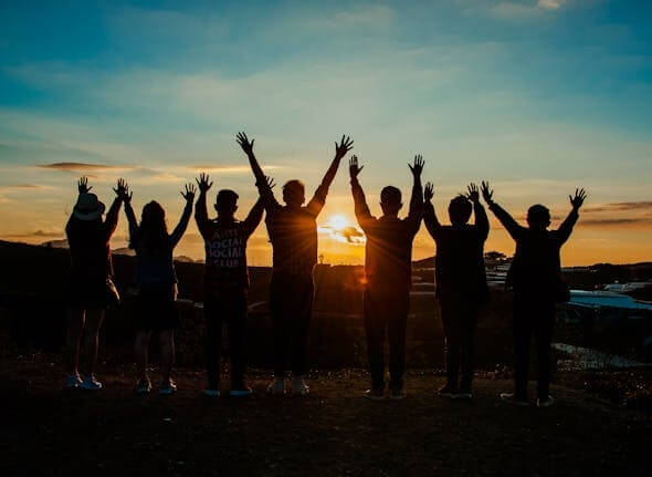 a group of people jumping happily looking at the sunset.