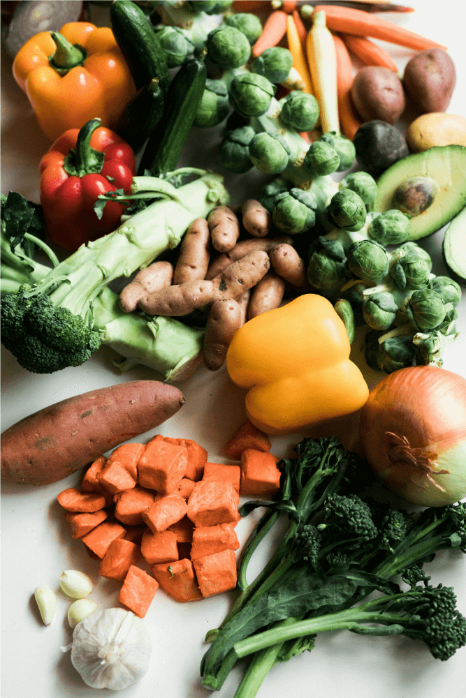 healthy eating image 2 A top down view of a lot of vegetables piled on a table. Carrots, broccoli, onions, peppers, Brussel sprouts, avocados, and sweet potatoes are all visible.