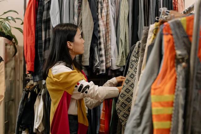 a woman with dark hair looking through rails of second hand clothes
