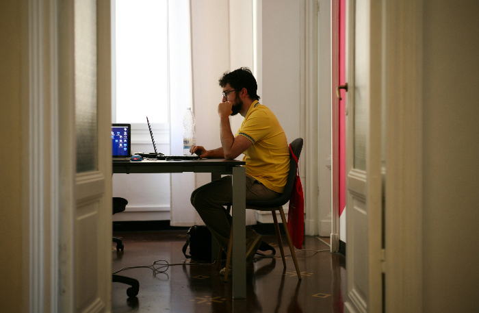 a man in a room sitting behind a desk on a laptop