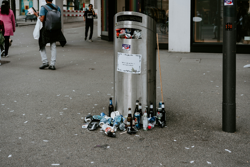 an overflowing bin with waste around in in a city area