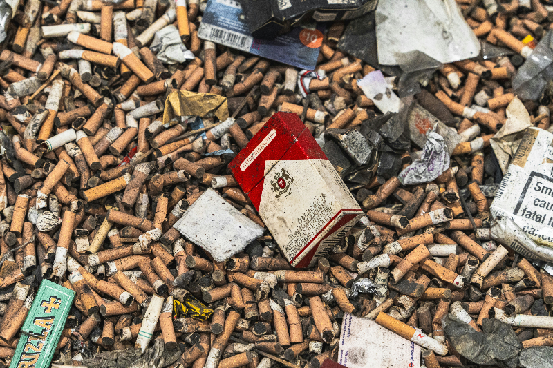 a lot a cigarettes on the ground along with litter