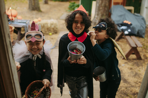Children outside a door trick or treating with a bucket of sweets in hand