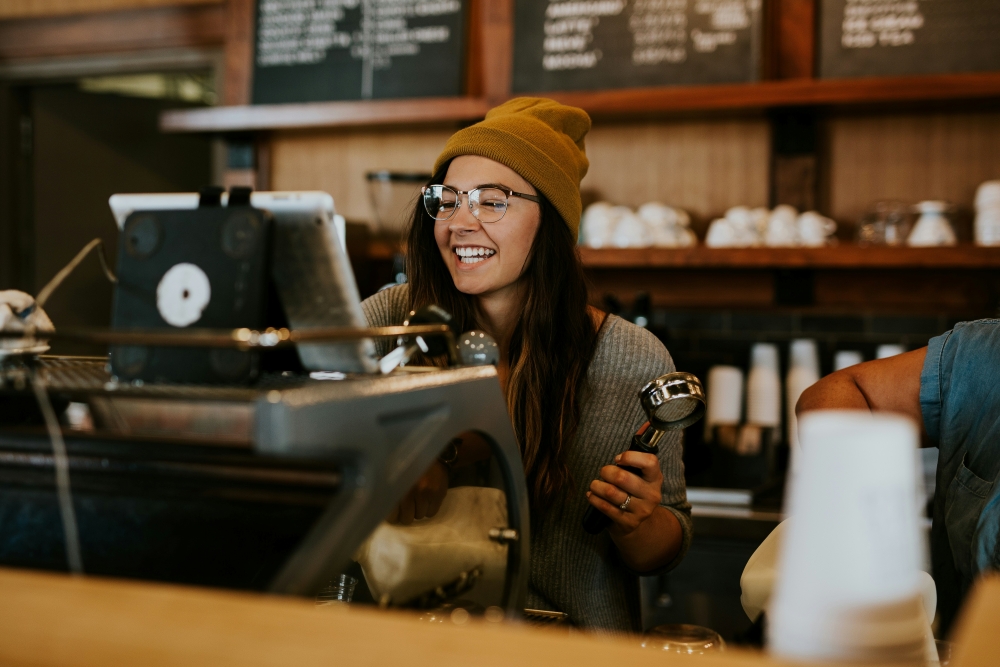 A smiling worker makes a coffee behind the bar in a cafe