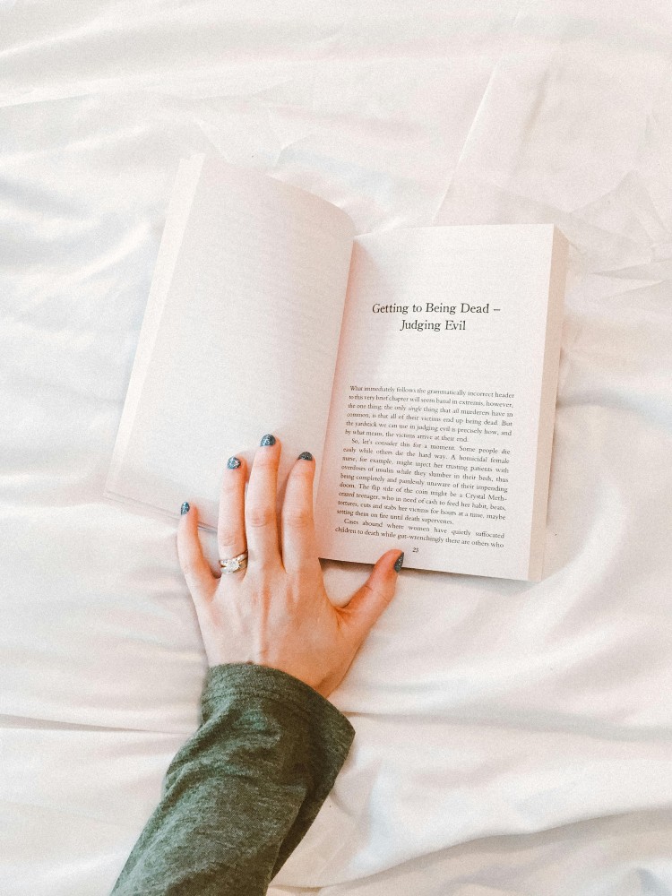 A woman's hand holding a book open on a bed